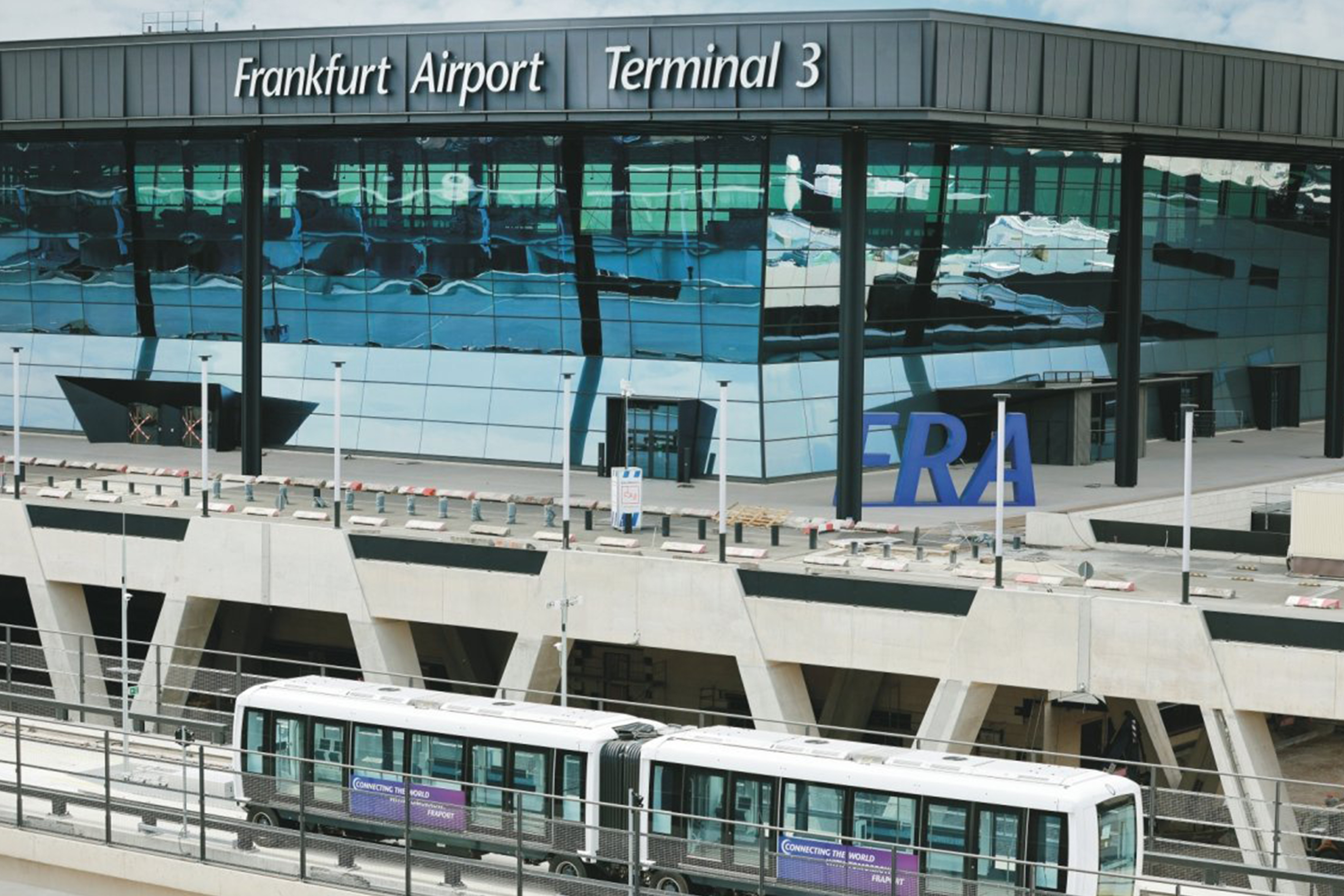 Au&szlig;enansicht des Frankfurt Airport Terminal 3 mit moderner Glasfassade, gut sichtbarer Beschriftung &bdquo;Frankfurt Airport Terminal 3&ldquo; und automatischer Skyline-Bahn vor dem Terminalgeb&auml;ude
